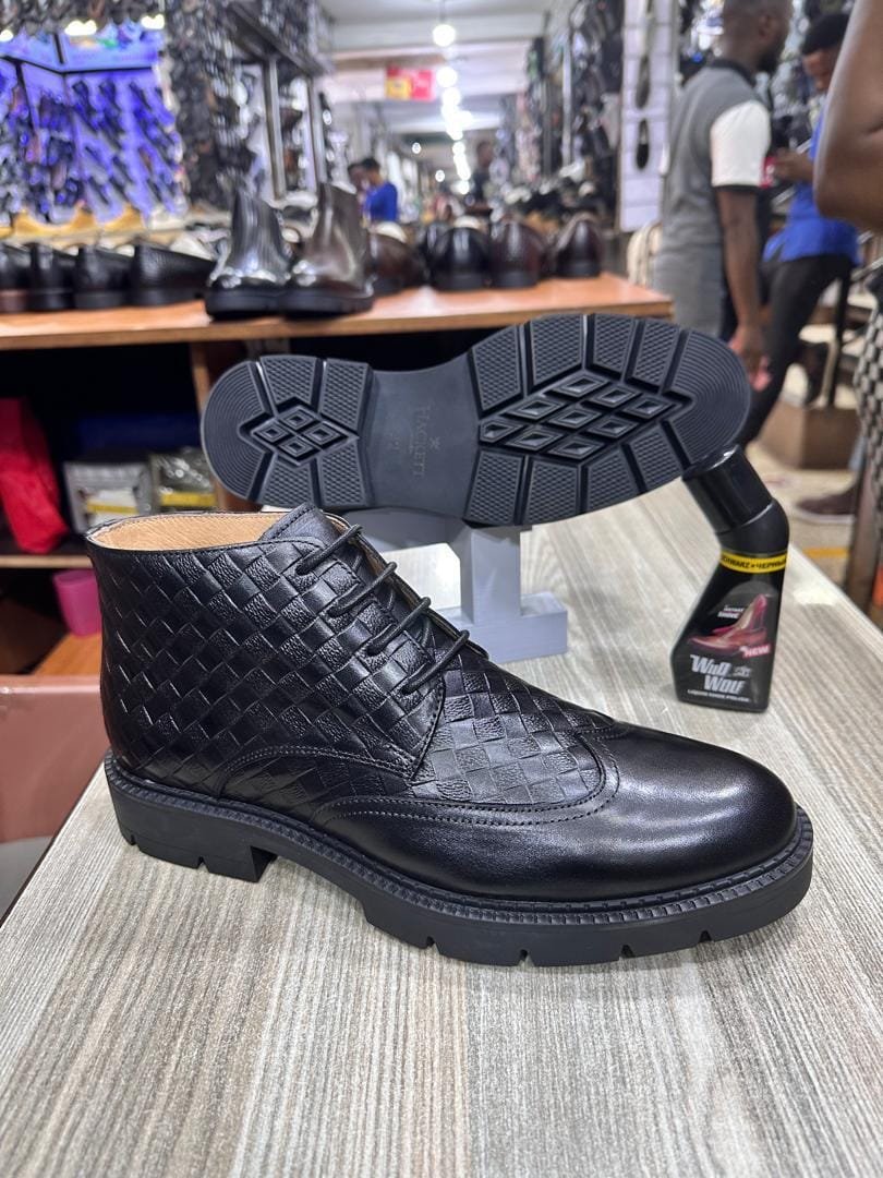 a black, leather, wingtip-style boot with a woven pattern on the ankle area